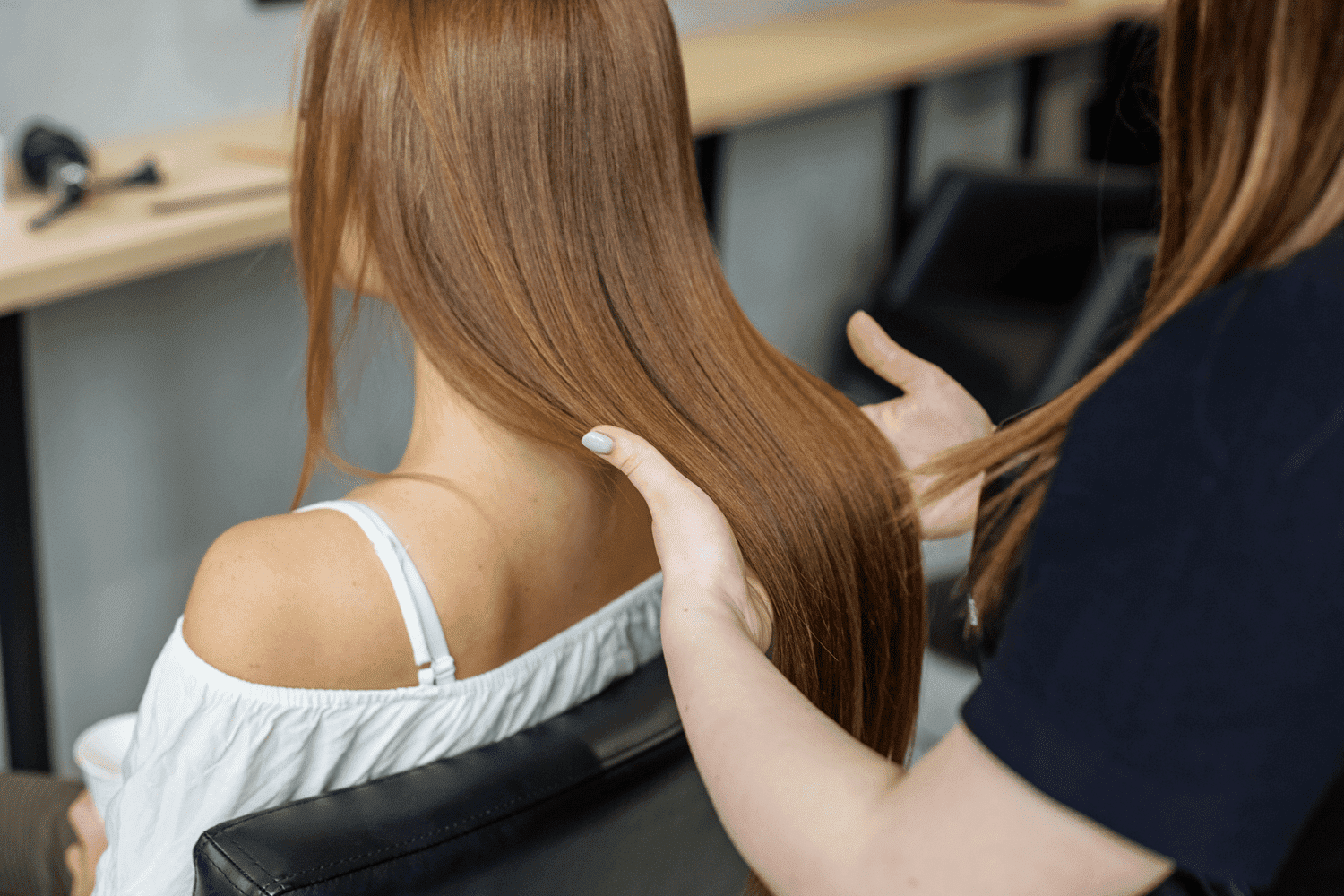 A hairstylist runs hands through a client's long, straight brown hair in a modern salon.