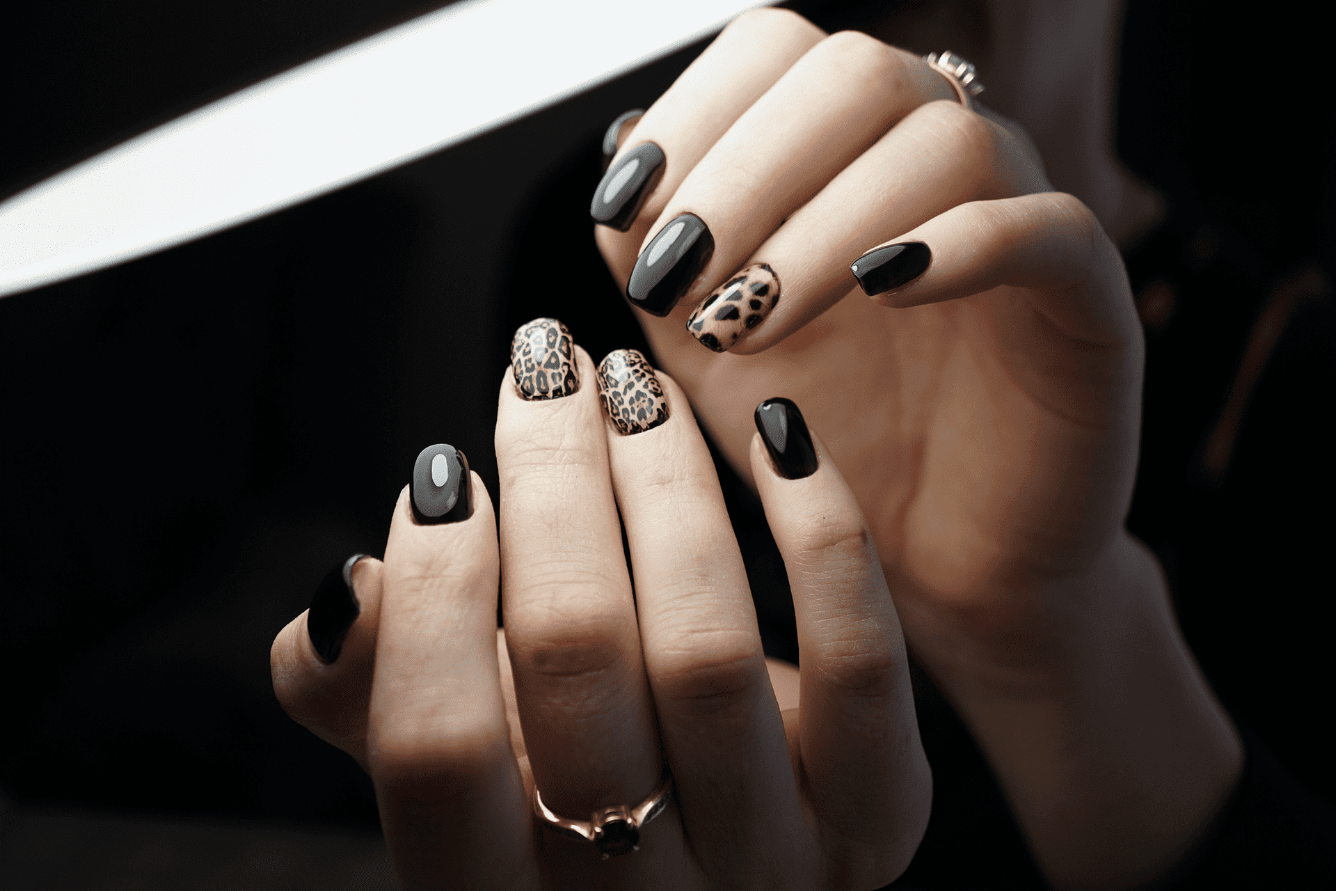 Close-up of hands with black and leopard print nail art, showcasing a stylish and trendy manicure.